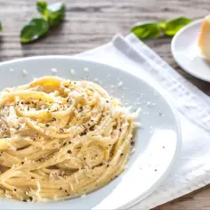 Szybki obiad z makaronem: spaghetti posypane parmezanem i pieprzem, obok kawałek sera i listki bazylii.