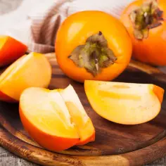 Pomarańczowe owoce kaki, pokrojone w ćwiartki, leżą na drewnianej desce. Ich słodycz i bogactwo witamin to prawdziwe **owoc kaki właściwości**.