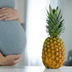 Brzuch kobiety w ciąży obok dojrzałego ananasa.