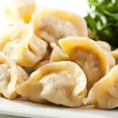 Pyszne, parujące pierogi z kapustą, ułożone na białym talerzu, z zieloną sałatką i czerwoną cebulą w tle.