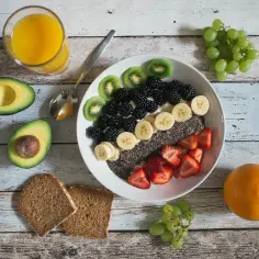 Zdrowe śniadanie: miska pełna owoców (truskawki, jeżyny, banany, kiwi), nasion chia, awokado, pełnoziarniste pieczywo i sok pomarańczowy. Idealne na dieta bez cukru.