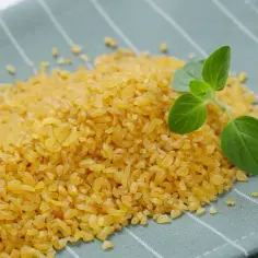 Kaszka bulgur na zielonym tle, z gałązką ziół. Niska kaloryczność i korzystny indeks glikemiczny sprawiają, że to zdrowy wybór.