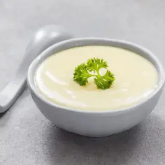 Kremowa zupa, idealna na dietę bezresztkową, ozdobiona natką pietruszki. Obok leży szara łyżka.