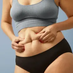 Kobieta z sylwetką skinny fat ściska fałdki tłuszczu na brzuchu.