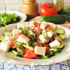 Pyszna sałatka z serem feta, pomidorem i ogórkiem, posypana szczypiorkiem. Idealna na lekki posiłek.