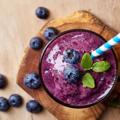 Jak zrobić smoothie? Pyszny, fioletowy koktajl z jagodami, ozdobiony świeżymi owocami i listkami mięty, z niebiesko-białą słomką.