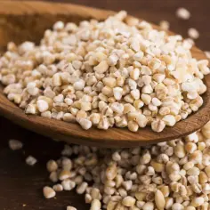 Kasza jęczmienna na drewnianej łyżce. Czy kasza jęczmienna ma gluten? Tak, jęczmień zawiera gluten.
