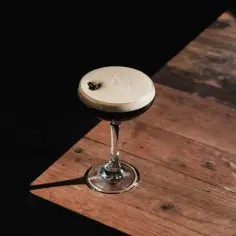 Idealny espresso martini przepis: koktajl z pianką i ziarnem kawy na drewnianym blacie.
