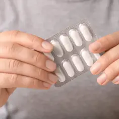 Dłonie trzymają opakowanie tabletek, które zapewnią dzienną dawkę magnezu.