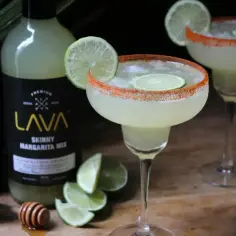 Dwa orzeźwiające drinki margharita z limonką i pikantnym brzegiem, obok butelki mieszanki LAVA.