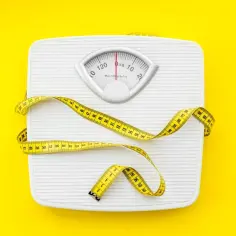 Biała waga łazienkowa z żółtą miarką, symbolizująca cel, jakim jest jak schudnąć 5 kg.