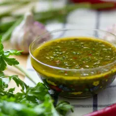 A miseczce lśni zielony sos chimichurri, obok świeża natka, czosnek i papryczka chili.