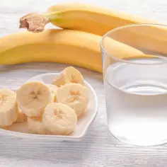 Pokrojony banan na talerzyku w kształcie serca i szklanka wody. Idealny banan na noc dla spokojnego snu.