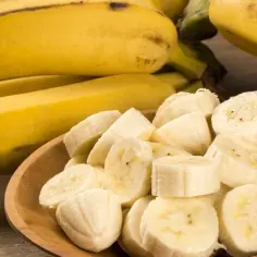 Całe i pokrojone banany na drewnianym tle. Poznaj bogactwo bananów i ich wartości odżywcze.
