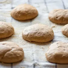 Surowe bułeczki na lnianym ręczniku, przygotowane do pieczenia. Zastanawiasz się, ile kcal ma kajzerka?