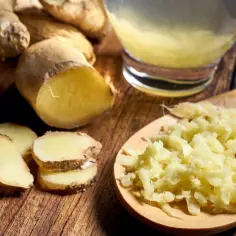 Świeży imbir w kawałkach i starty na łyżce, obok szklanki napoju. Czy imbir szkodzi na jelita? Zwykle nie, a wręcz pomaga.