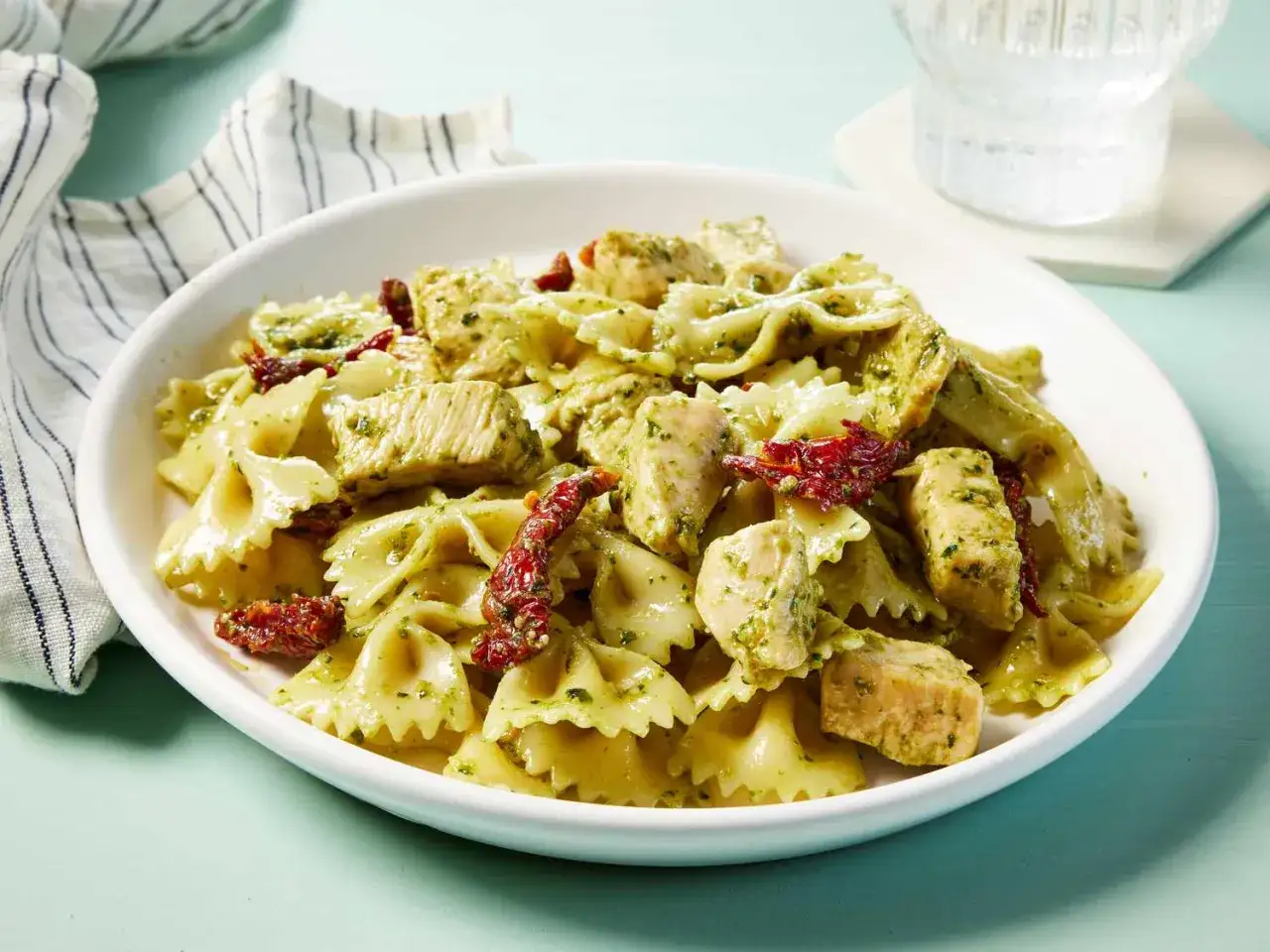 Pyszny makaron z pesto ze słoika i kawałkami kurczaka, ozdobiony suszonymi pomidorami. Szybki i prosty obiad.