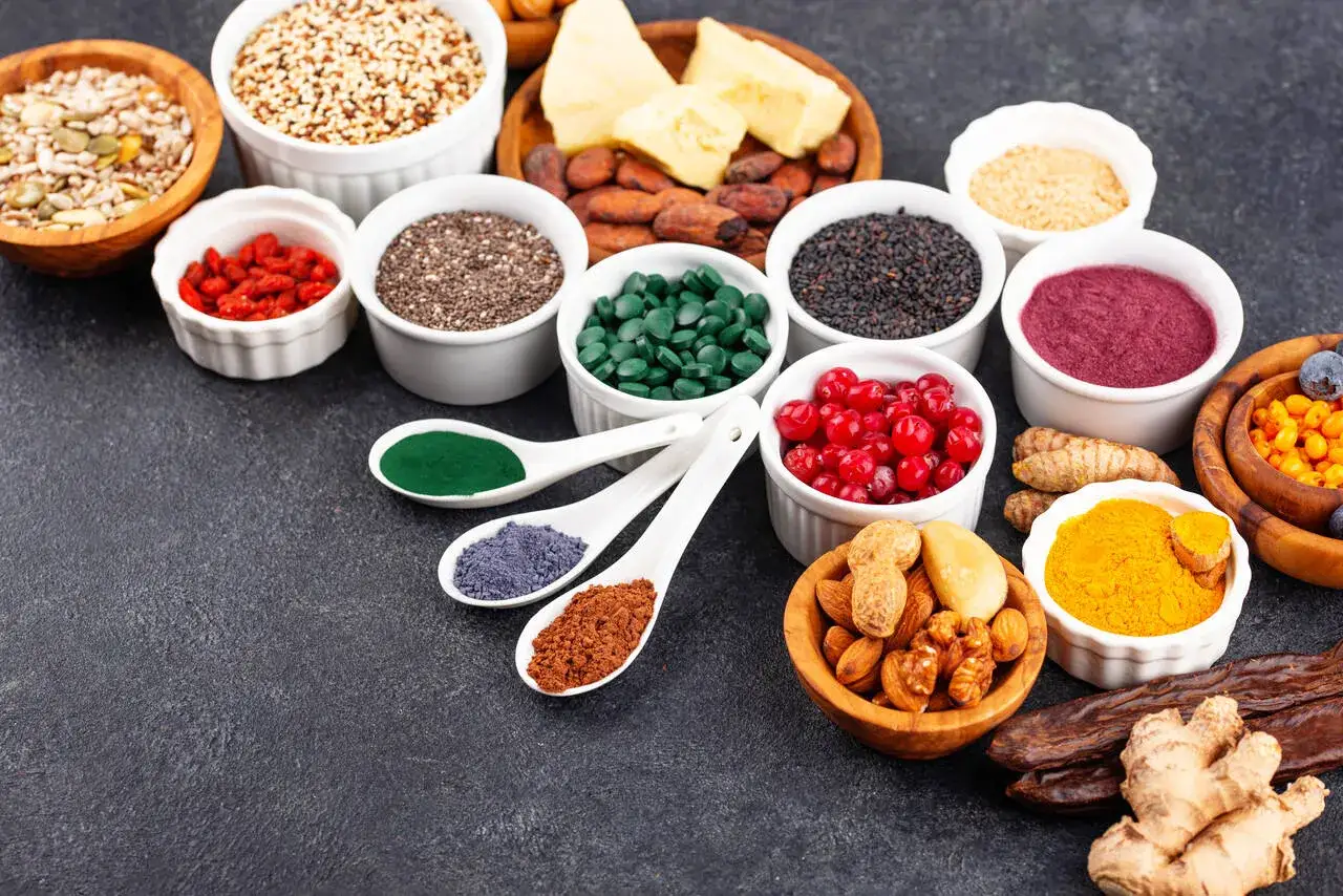 Miseczki z nasionami, jagodami goji, spiruliną, czarnuszką, owocami leśnymi i kurkumą. Wśród nich proszek z kakao, który jest dobrym źródłem fosforu.