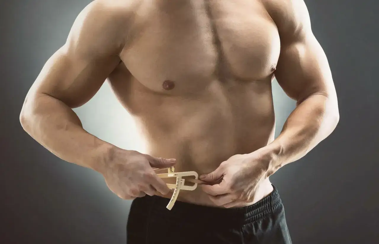 Mężczyzna z umięśnionym torsem mierzy obwód talii, by sprawdzić, czy nie ma sylwetki skinny fat.