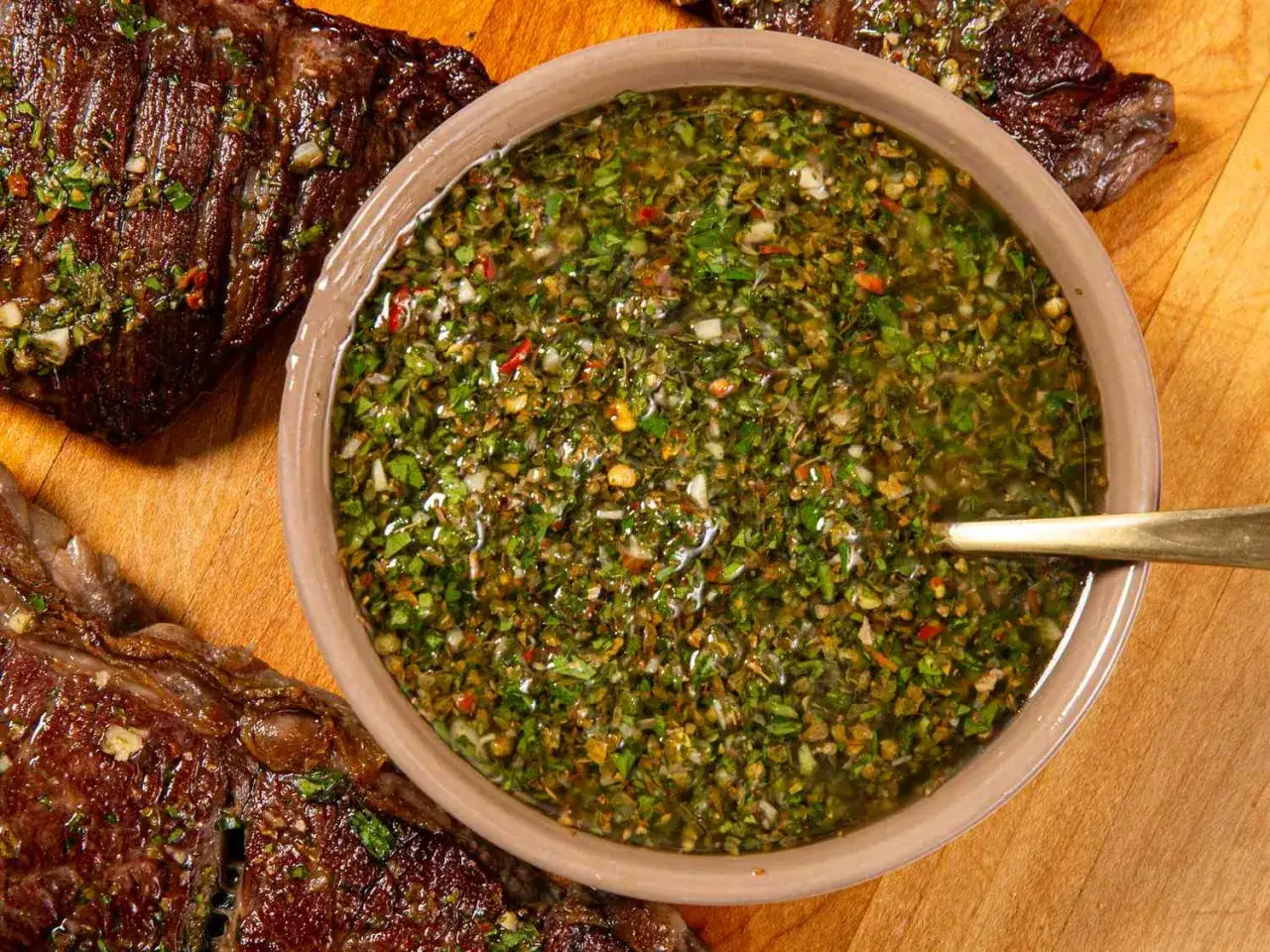 A miska pełna aromatycznego sosu chimichurri, obok soczyste, grillowane steki. Idealne połączenie smaków.