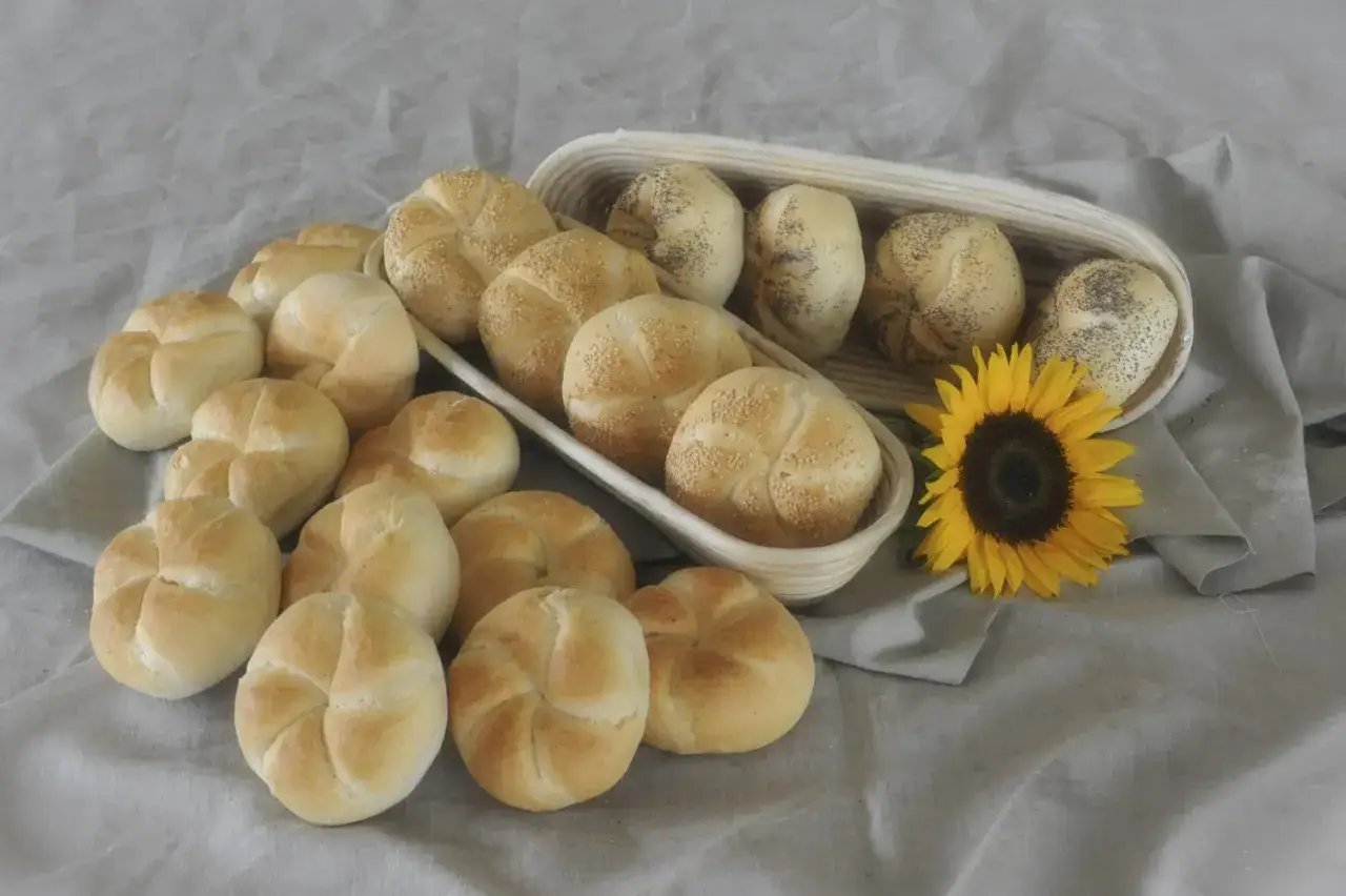 Świeże kajzerki, niektóre posypane sezamem, inne makiem, leżą obok słonecznika. Ile kcal ma kajzerka?