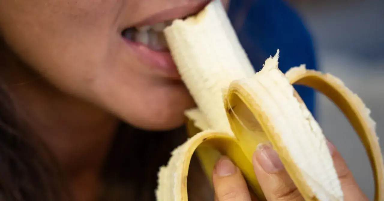 Kobieta gryzie banana. Czy cukrzyk może jeść banany? Tak, ale z umiarem, bo to źródło cukrów.