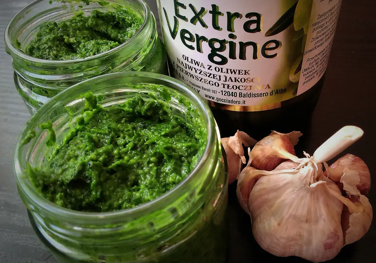 Pesto z jarmużu w słoiczkach, obok czosnek i butelka oliwy Extra Vergine.