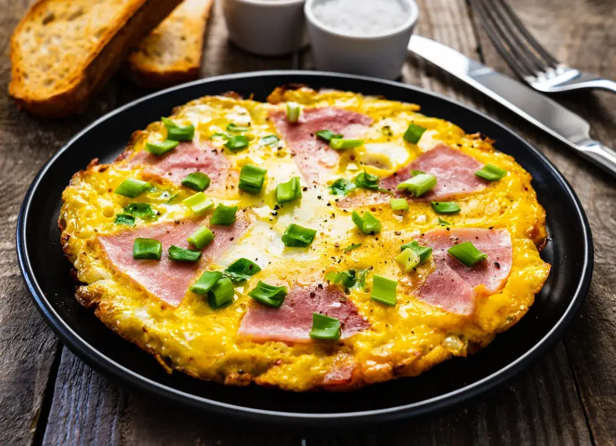 Pyszny omlet z szynką i serem, posypany szczypiorkiem. Idealny pomysł, jak zrobić omlet z szynką i serem na śniadanie.