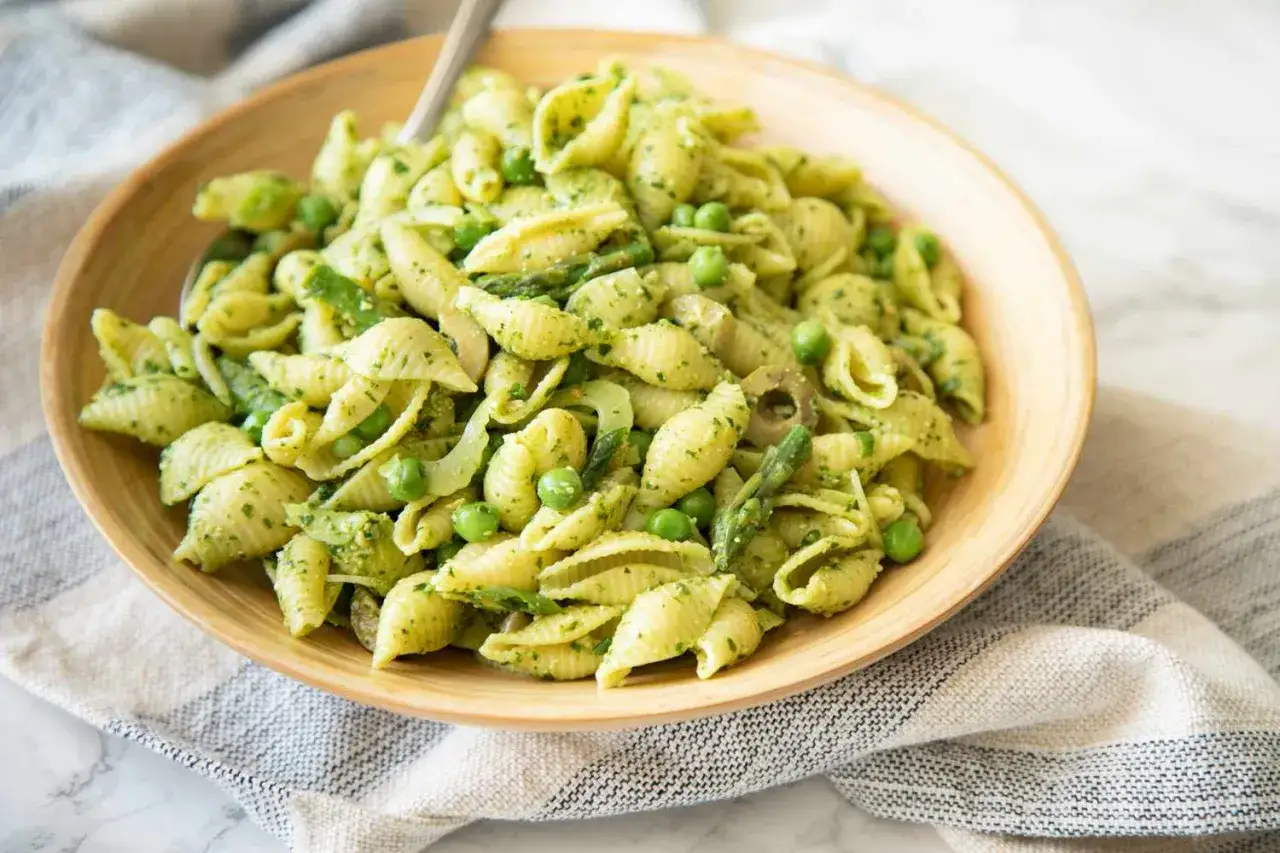 Szybki obiad z makaronem w sosie pesto, z groszkiem i szparagami, podany w drewnianej misce.