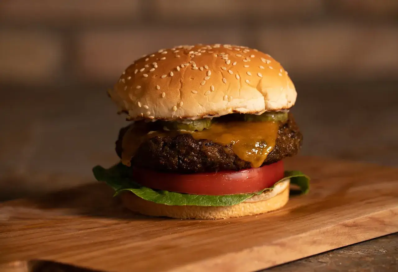 Soczyste burgery z grilla, z topniejącym serem i chrupiącą sałatą, na desce z drewna.