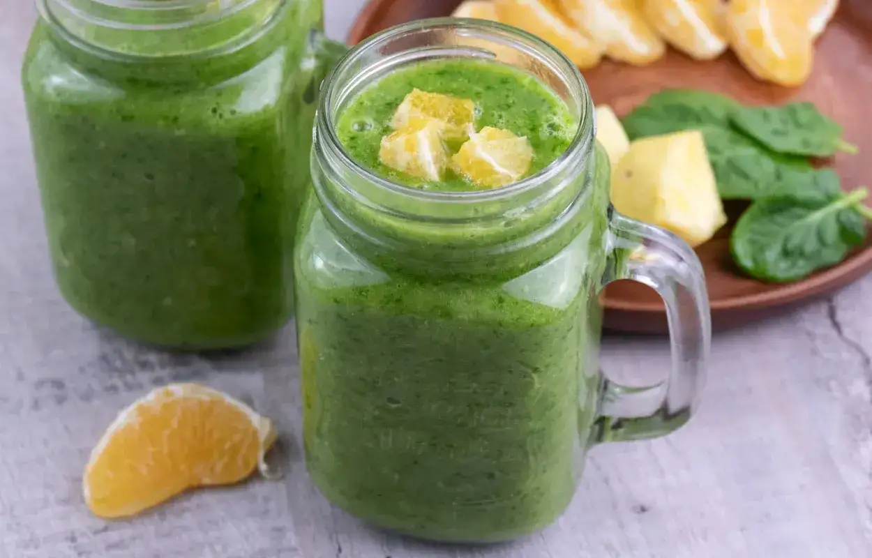 Zielony smoothie w słoiku, ozdobione kawałkami pomarańczy. Idealny przepis na to, jak zrobić smoothie pełne witamin.