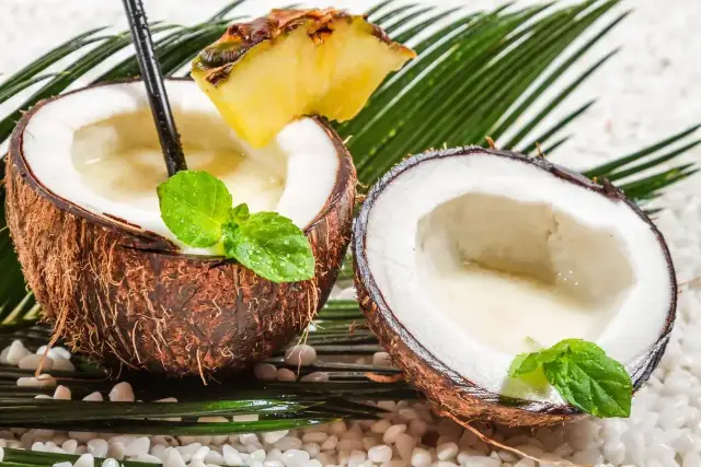 Dwa połówki kokosa z napojem, ozdobione miętą i ananasem. Czy kokos to owoc? Tak, i jest idealny na tropikalny drink!