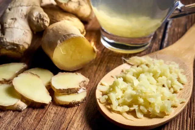 Świeży imbir w kawałkach i starty na łyżce, obok szklanki napoju. Czy imbir szkodzi na jelita? Zwykle nie, a wręcz pomaga.